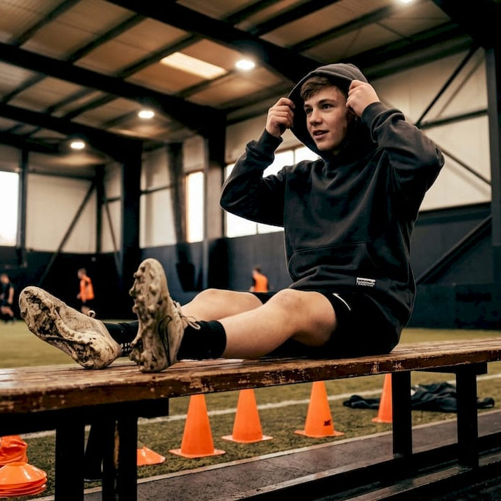 Youth athlete wearing sweatshirt on bench outdoors