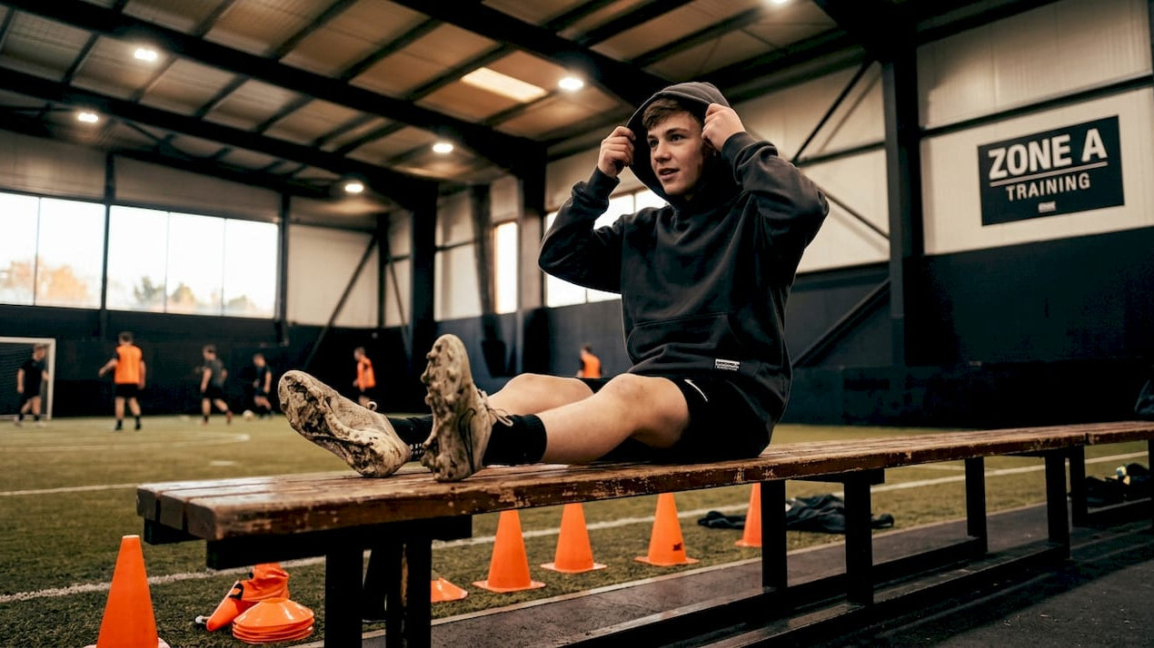 Youth athlete wearing sweatshirt on bench outdoors