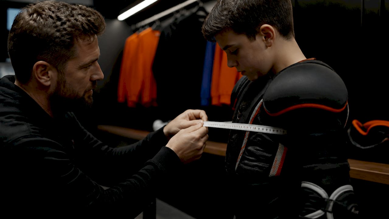 Coach measuring player chest with pads